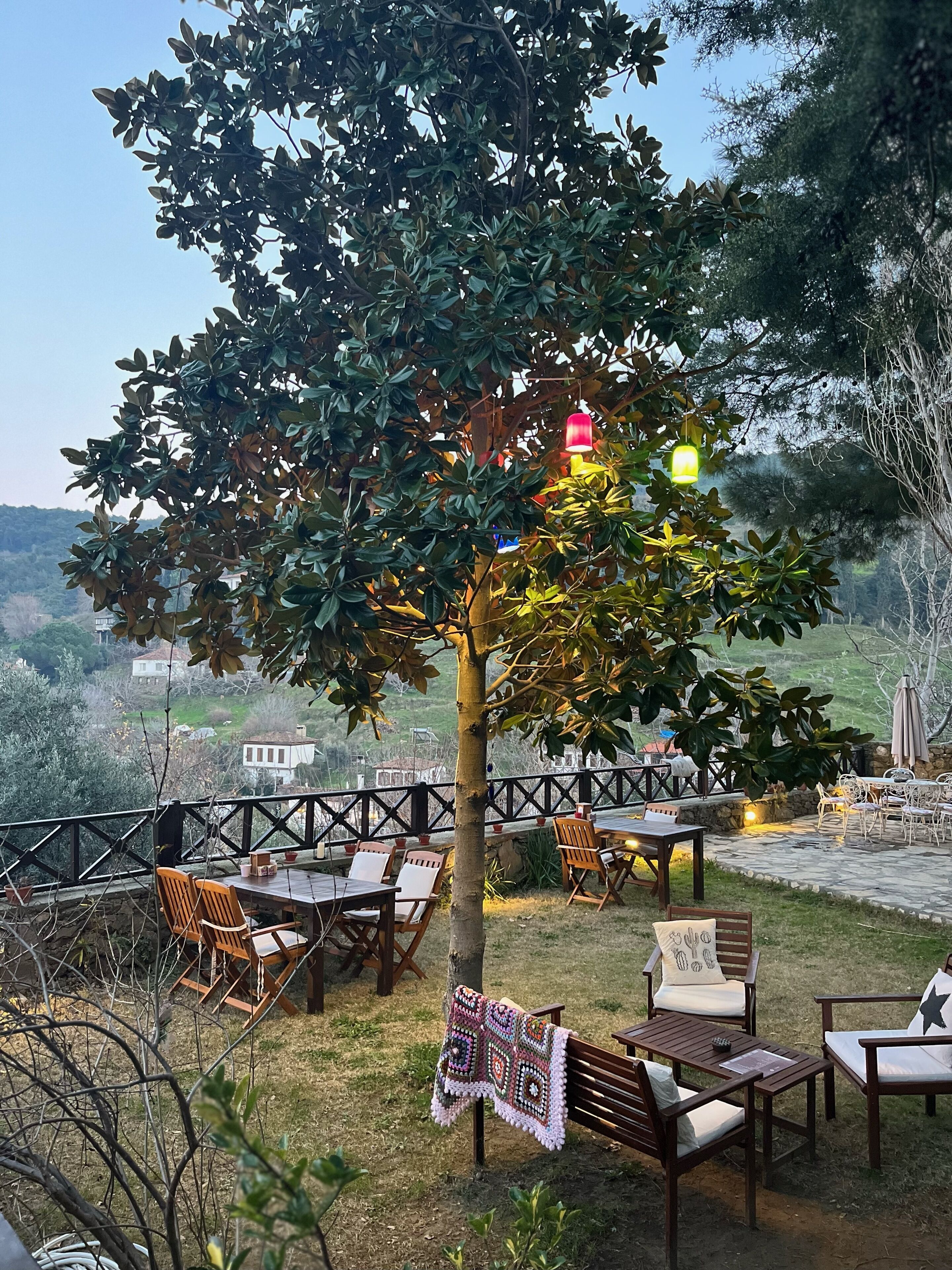 An outdoor seating area with wooden furniture, a tree, and a view of the countryside.
