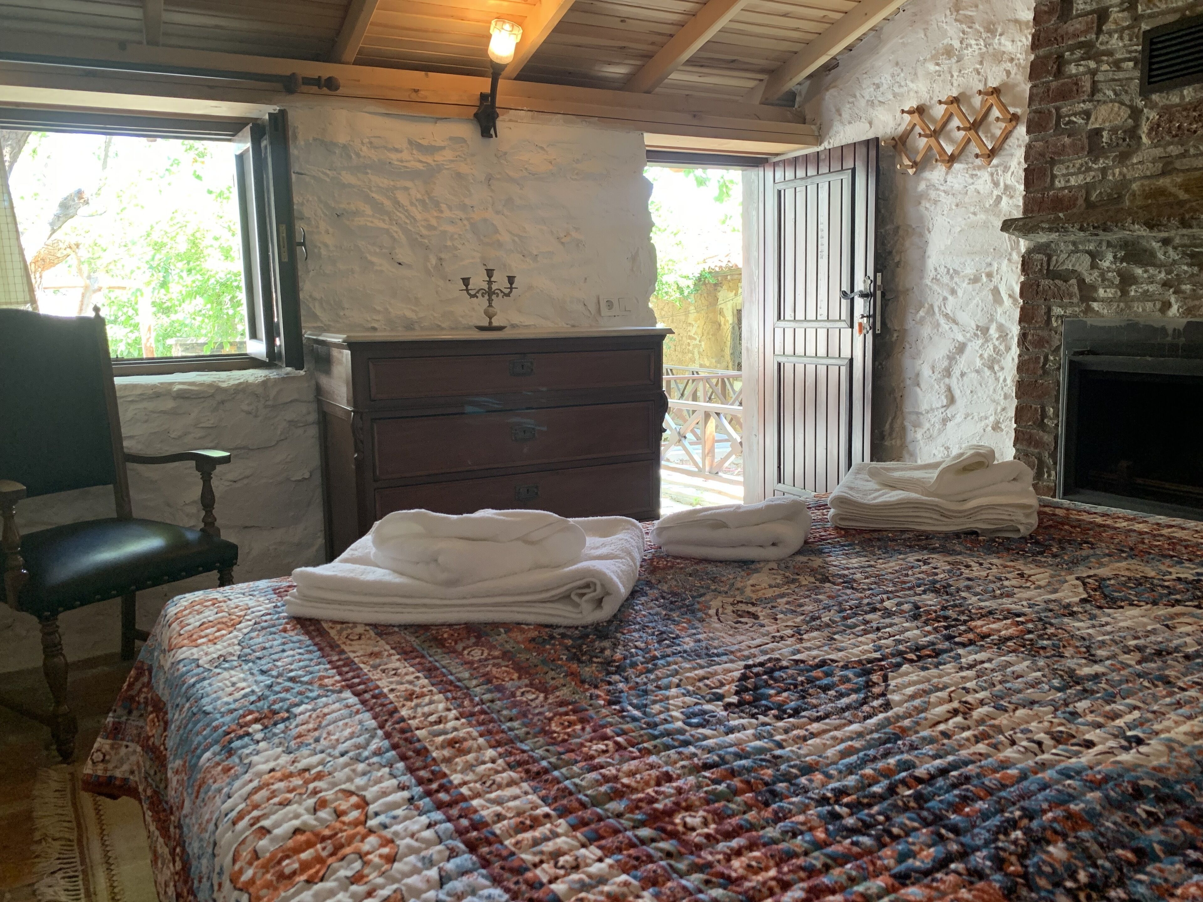 A bedroom with a bed, a dresser, a chair, a fireplace, and a view of the outdoors.