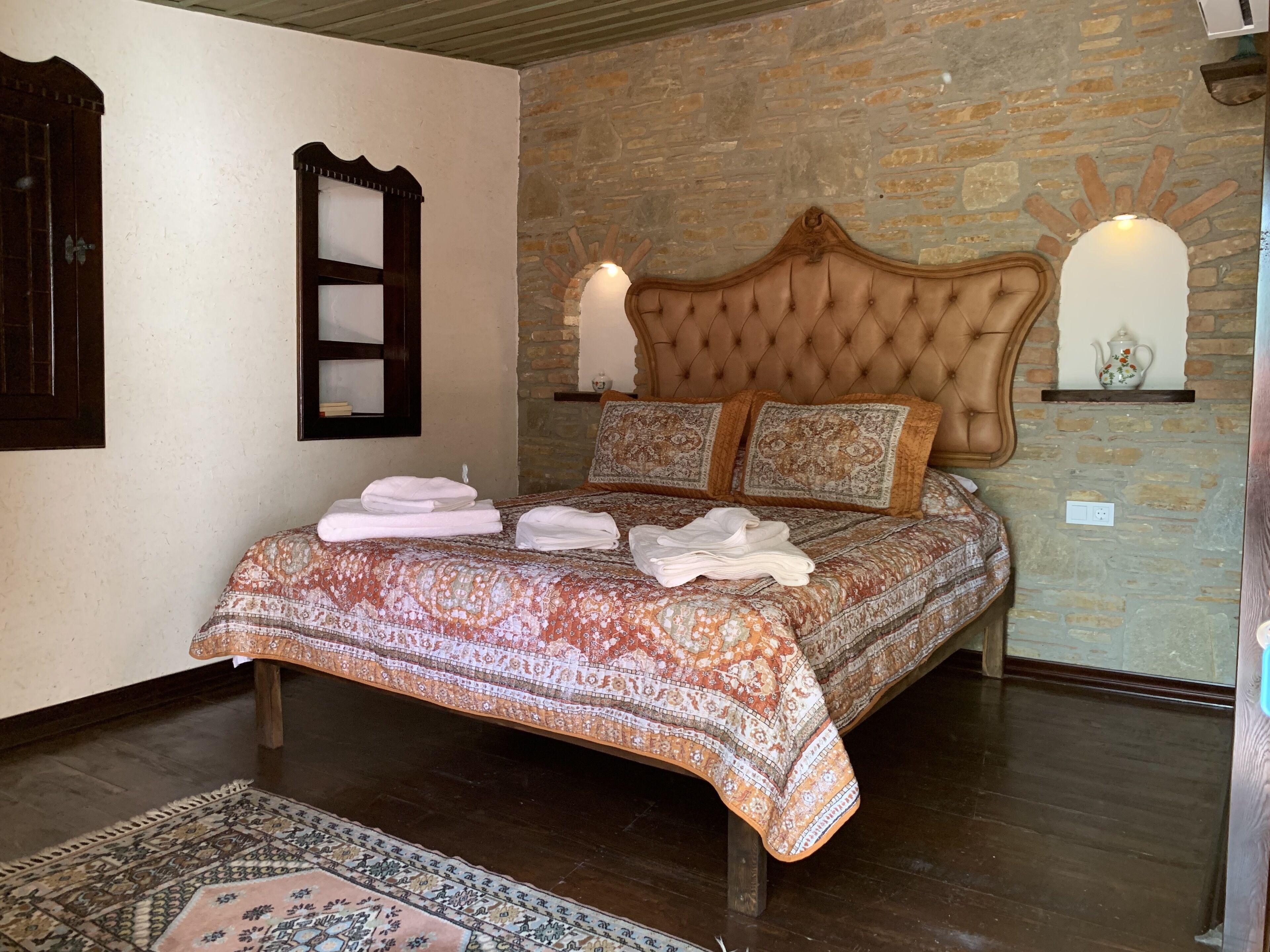Une chambre à coucher avec une couvre-lit à motifs, une tête de lit capitonnée et un mur en pierre.