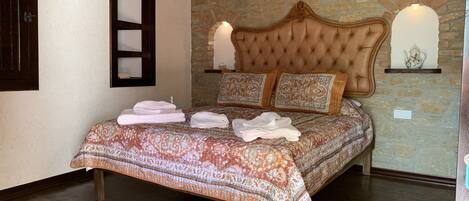 A bedroom with a patterned bedspread, a tufted headboard, and a stone wall.