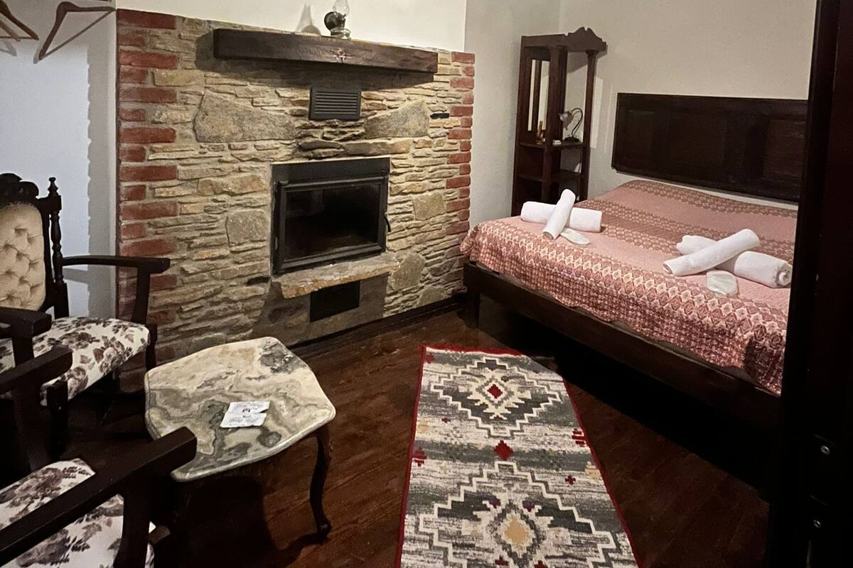 A cozy room with a stone fireplace, a bed with a red blanket, a patterned rug, and a wooden ceiling.