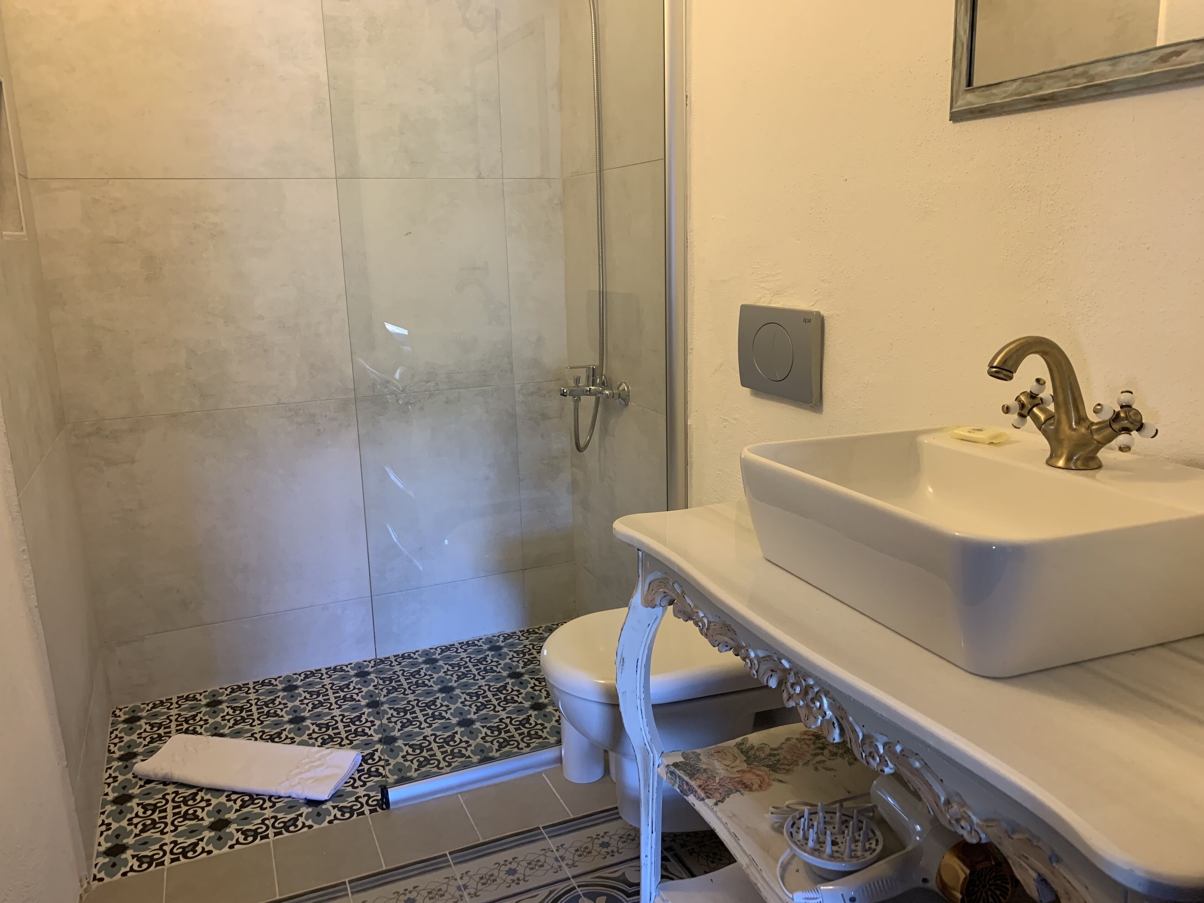 A bathroom with a shower, toilet, sink, and a patterned floor.