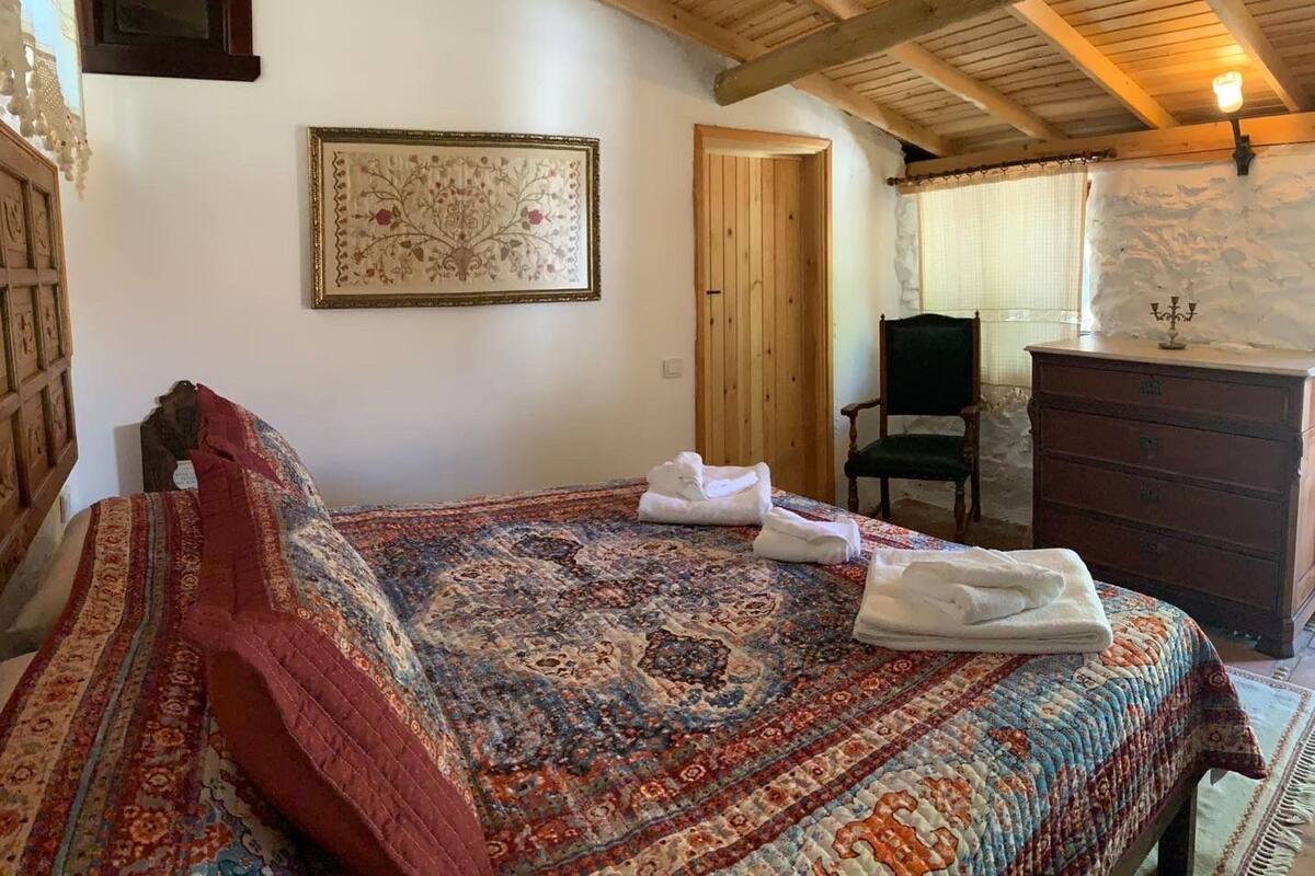 A bedroom with a bed, a wooden dresser, a chair, and a framed picture on the wall.