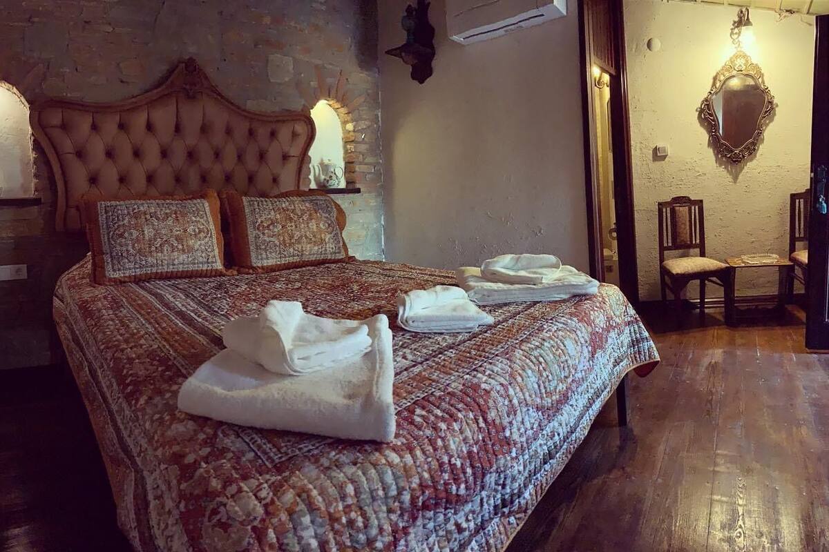 A bedroom with a large bed, a stone wall, and a wooden floor.