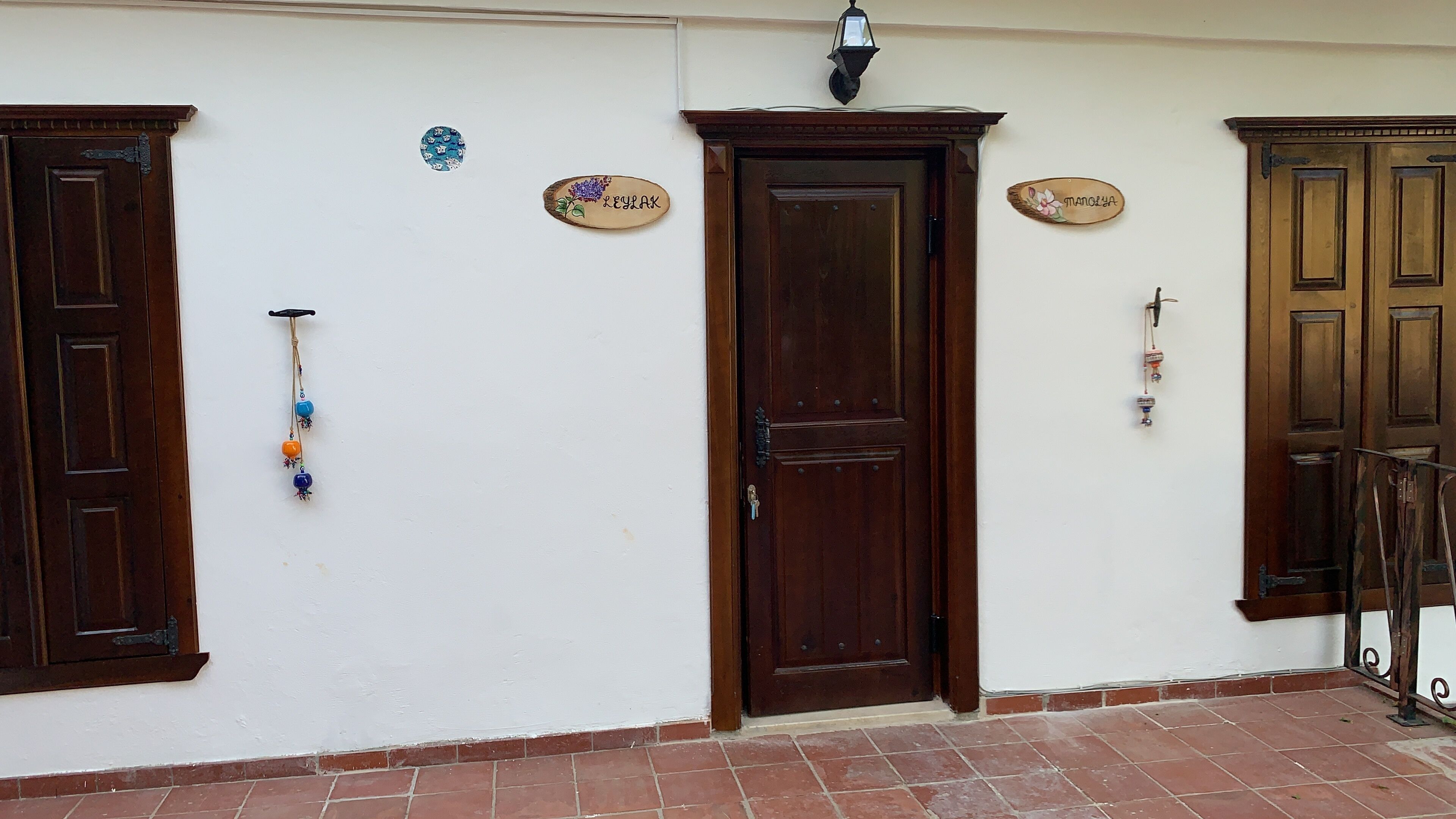 Fachada de edificio con dos puertas de madera, un aplique y tres placas con nombres.