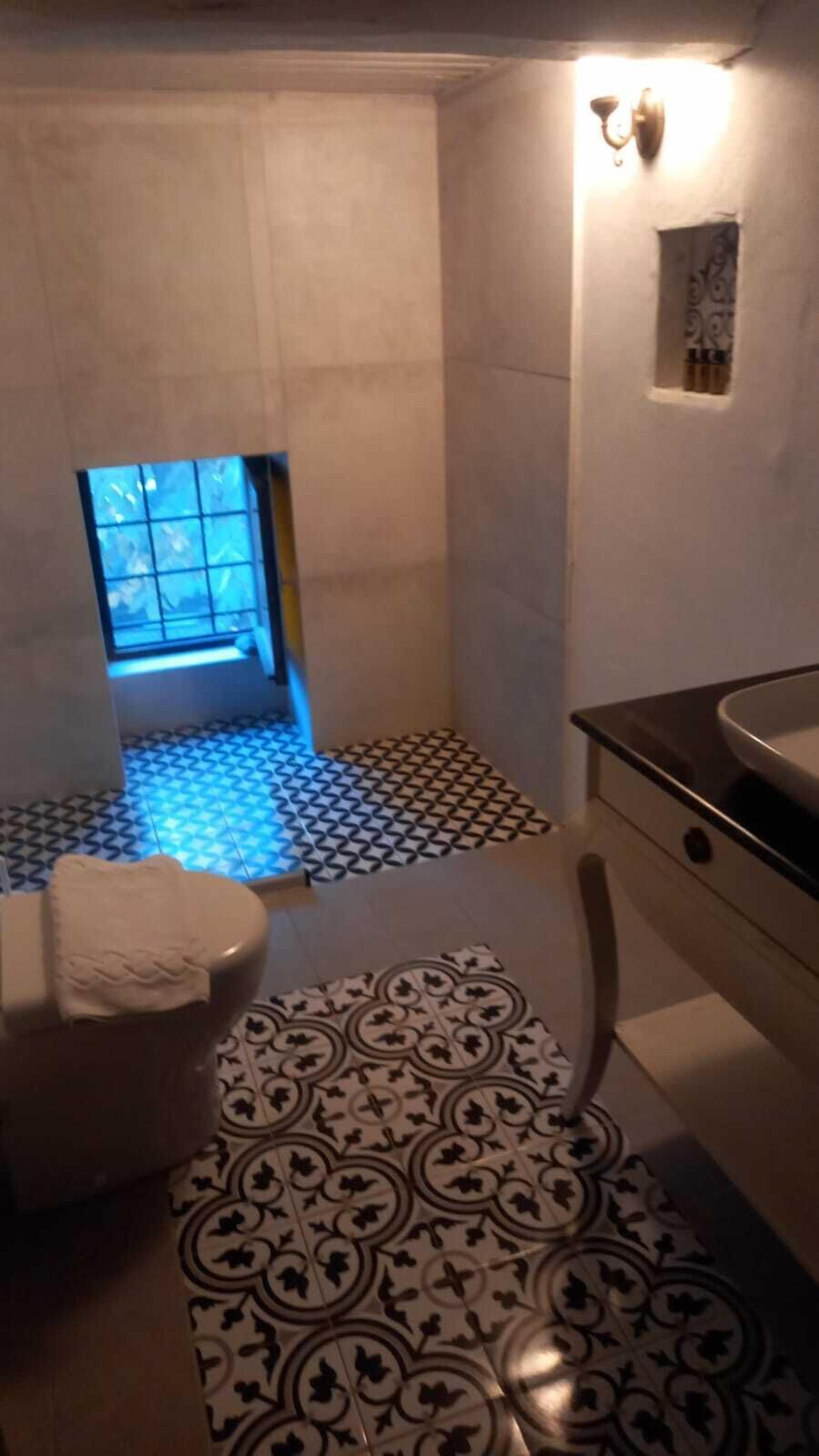 A bathroom with a patterned floor, a toilet, a sink, and a shower area with a small window.