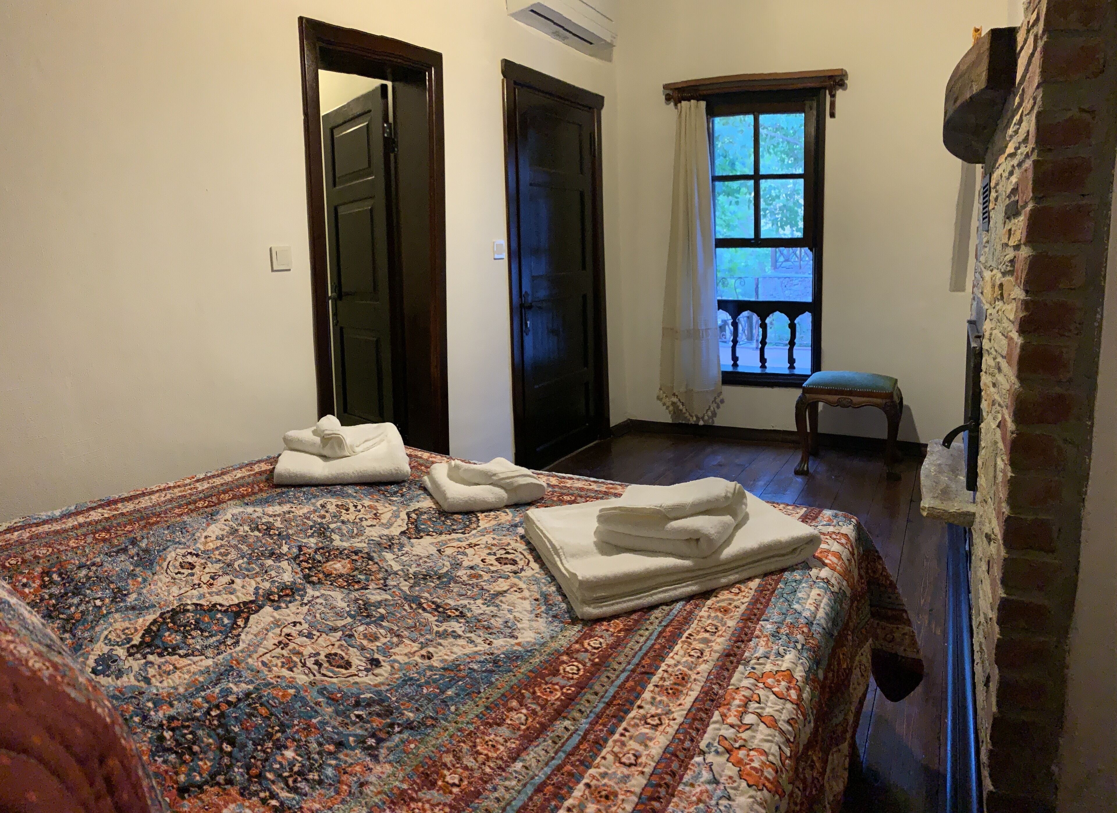 A bedroom with a large bed, two doors, a window with a view, and a small chair.