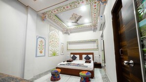 Quarto com cama, dois banquinhos coloridos, uma escrivaninha e uma porta.