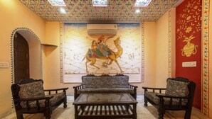 Quarto com decoração tradicional, apresentando um mural de parede estampado, um sofá central e duas poltronas.