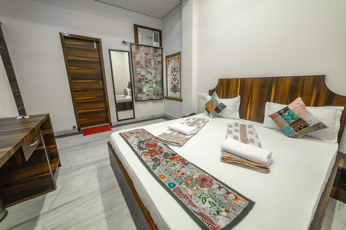 Un dormitorio ordenado con cabecera de madera, una cama grande con múltiples almohadas y un corredor decorativo, un escritorio de madera y un espejo en la pared.