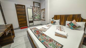 Un dormitorio ordenado con cabecera de madera, una cama grande con múltiples almohadas y un corredor decorativo, un escritorio de madera y un espejo en la pared.