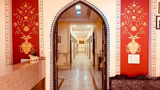 Um hall de hotel com uma receção de mármore, um sofá estampado e um corredor com parede vermelha e padrão floral.