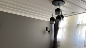 Ein Schlafzimmer mit einem großen Bett, einem Nachttisch, einer Lampe, einem Fenster mit Vorhängen und einer Deckenleuchte.