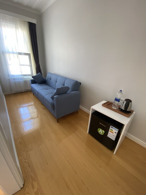 A room with a blue sofa, a small white table with a water bottle and kettle, and a refrigerator with an A+ sticker. - White Island Boutique Hotel (Adalar)