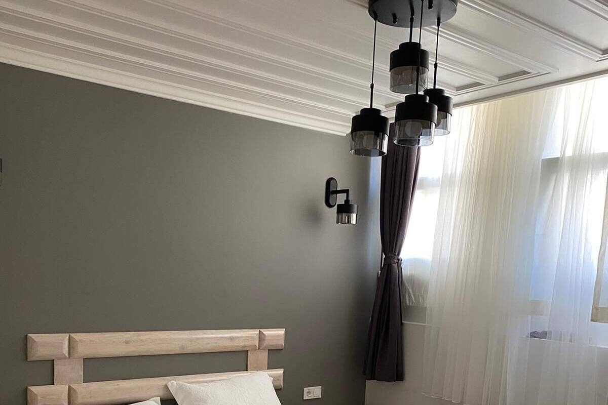 Ein Schlafzimmer mit einem großen Bett, einem Nachttisch, einer Deckenleuchte und einem Fenster mit Vorhängen.