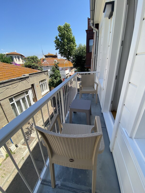 A balcony with wicker chairs, a small table, and a view of neighboring buildings and trees. - White Island Boutique Hotel (Adalar)