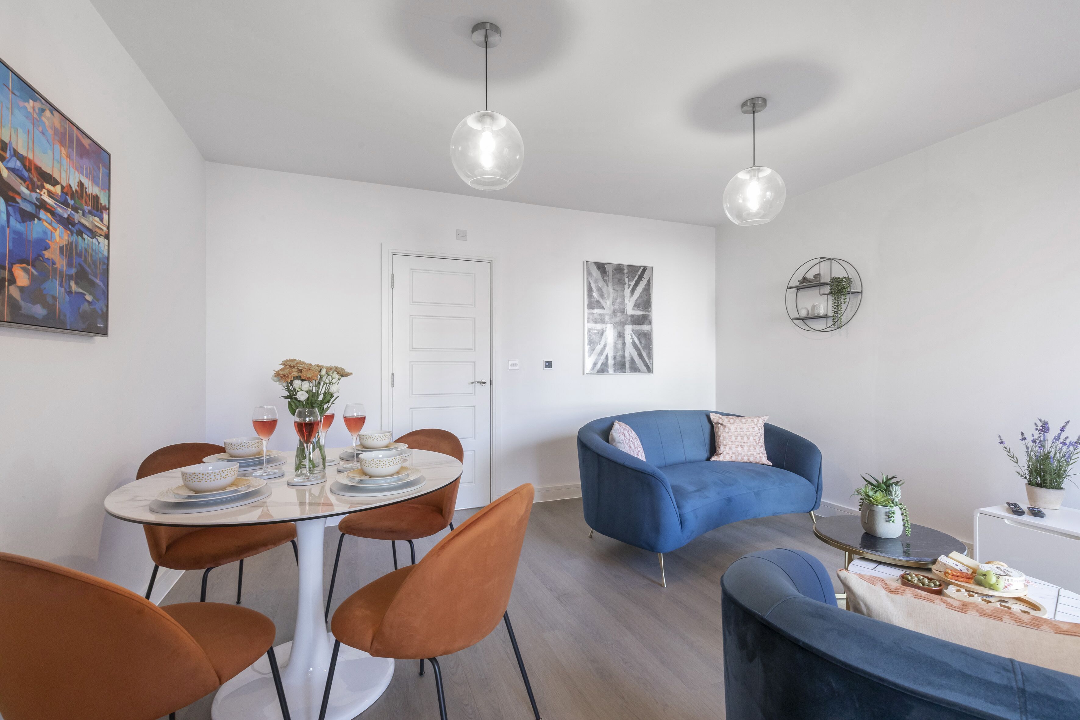 A modern living room with a blue sofa, a dining table with chairs, and pendant lights.