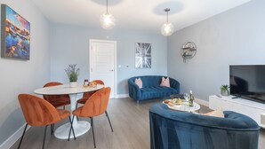 A modern living room with a dining area, a sofa, and a TV. - Elliot Oliver - Cosy 2 Bedroom Town Centre Apartment (Cheltenham)