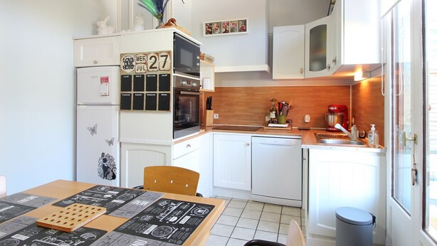 Cocina compacta con armarios blancos, horno integrado y zona de comedor con mesa para dos.