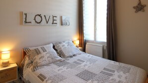 Un dormitorio con cama, dos lámparas de noche, una ventana con cortinas y un adorno en la pared que dice 'LOVE'.