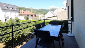 Un balcón con mesa y sillas, con vista a una zona residencial con casas y colinas.