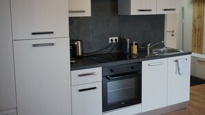 A modern kitchen with white cabinets, a black countertop, stainless steel appliances, and a wooden door. - HochgratBlick.modern.cozy.relaxed (Argenbühl)