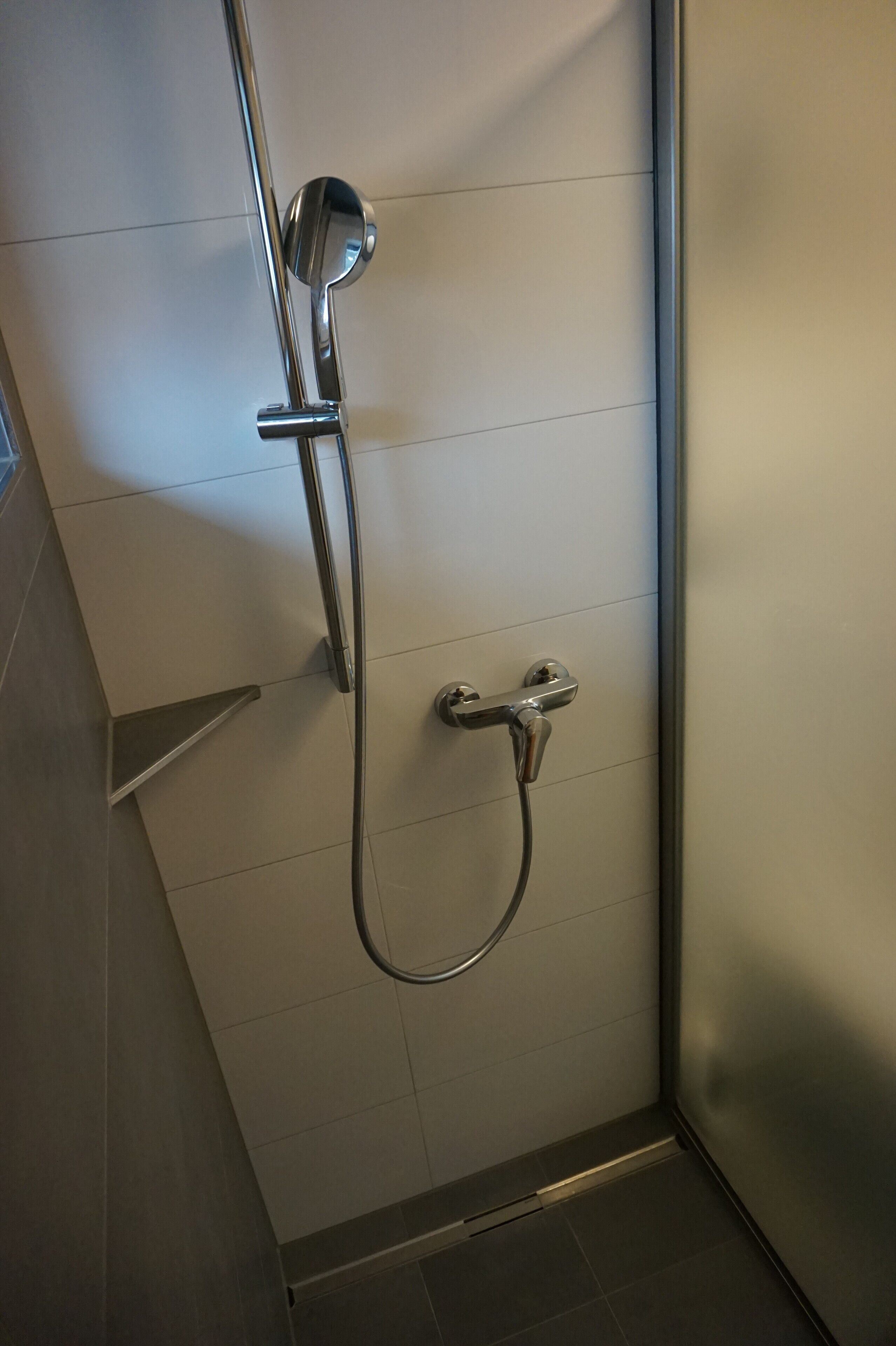 A shower with a handheld showerhead and a wall-mounted faucet.