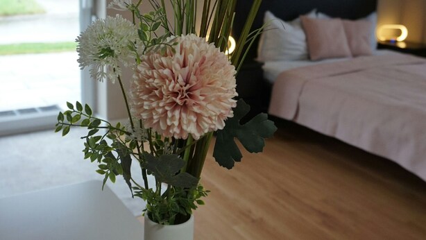 A room with a bed, a bedside table with a vase of flowers, and a window with a view of greenery. - HochgratBlick.modern.cozy.relaxed (Argenbühl)