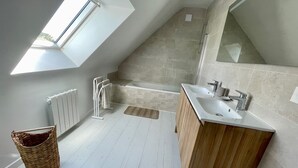Un baño moderno con tragaluz, una bañera, una ducha e un lavabo con lavamanos.