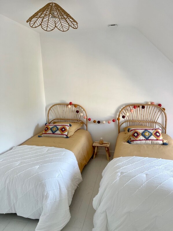 A bedroom with two beds, a hanging light fixture, and a small wooden table.