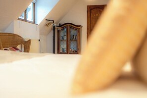 Une chambre avec un plafond en pente, une armoire en bois et une chaise en osier.