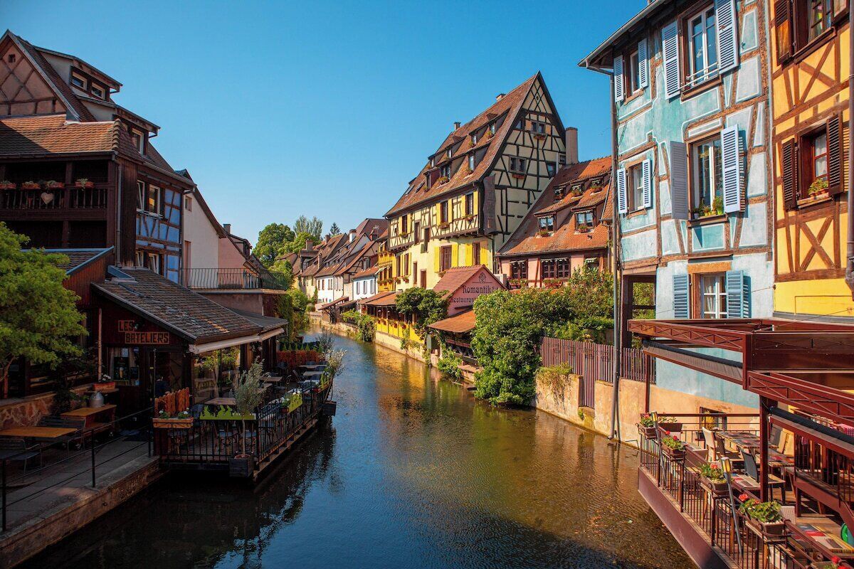 A narrow waterway flanked by traditional half-timbered buildings with outdoor seating areas.