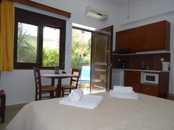 A room with a bed, a table with chairs, a kitchenette, and a sliding glass door to a balcony. - Lito Apartments (Kantanos-Selino)