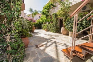 A stone-paved courtyard with potted plants, a wooden staircase, and a building with a beige facade.