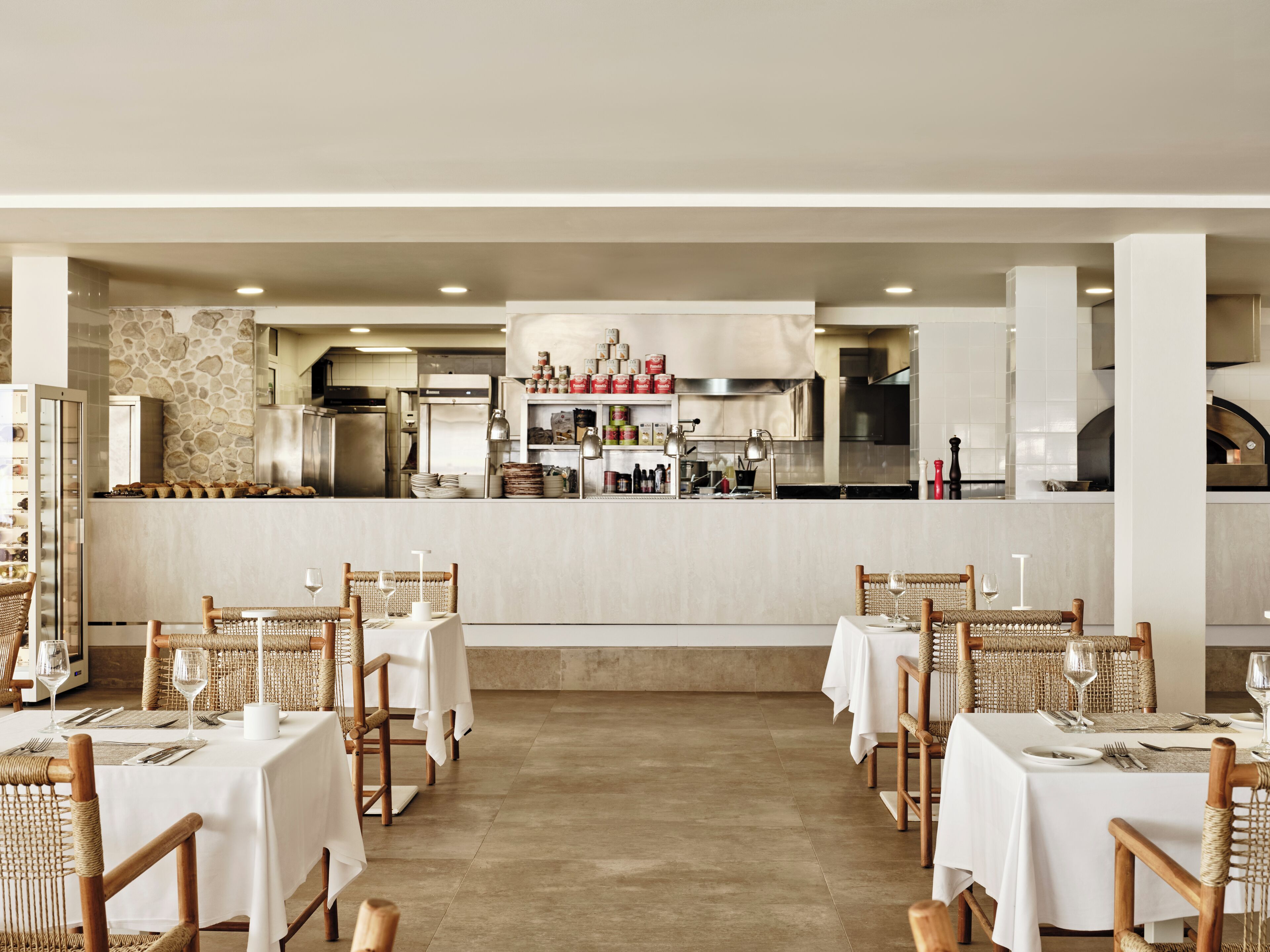 Un restaurant doté d’un bar central, de plusieurs tables recouvertes de nappes blanches et de chaises en osier.