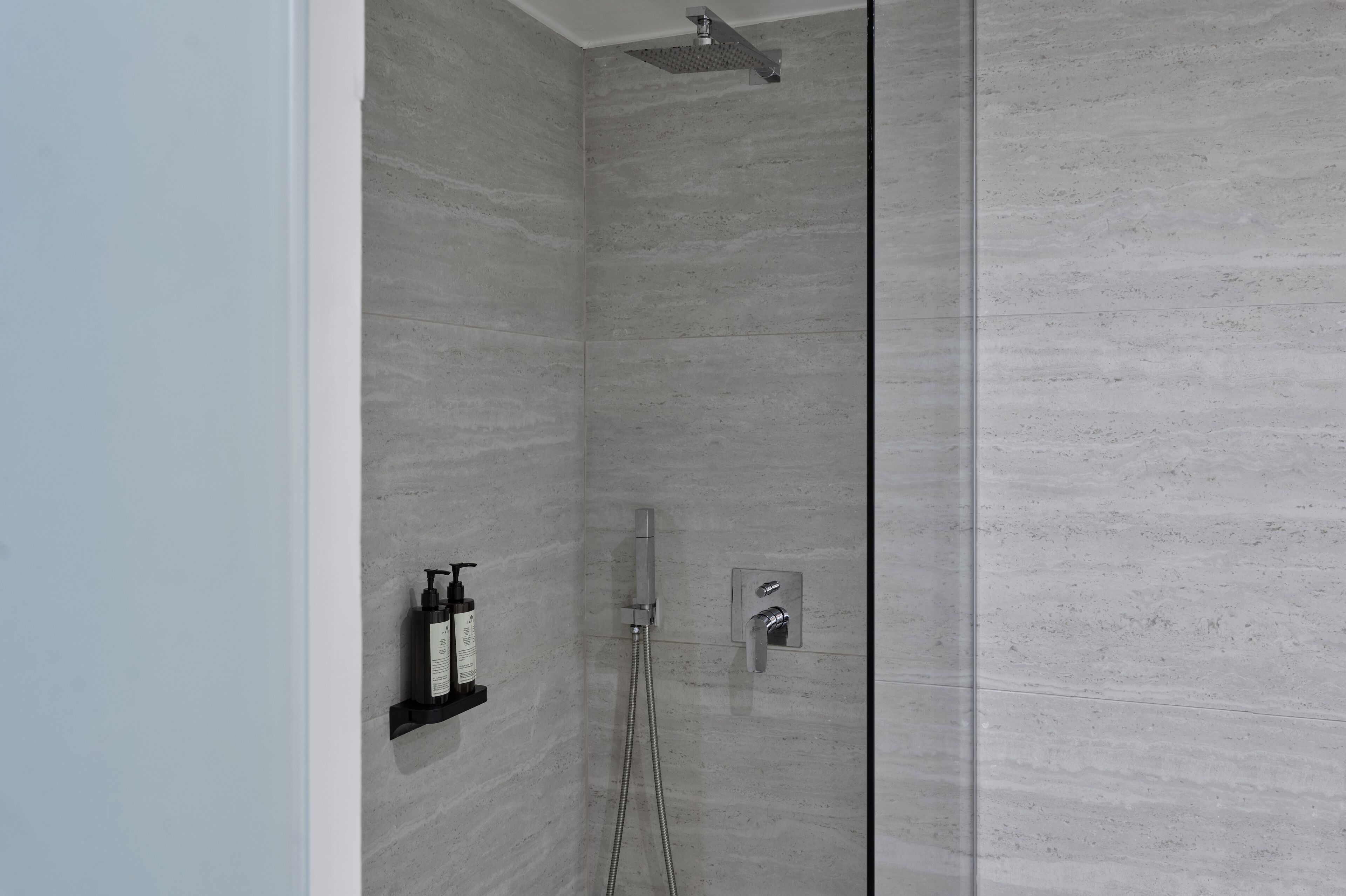 Eine moderne Dusche mit Glastür, Duschbrausehandstück und Armatur an der Wand.