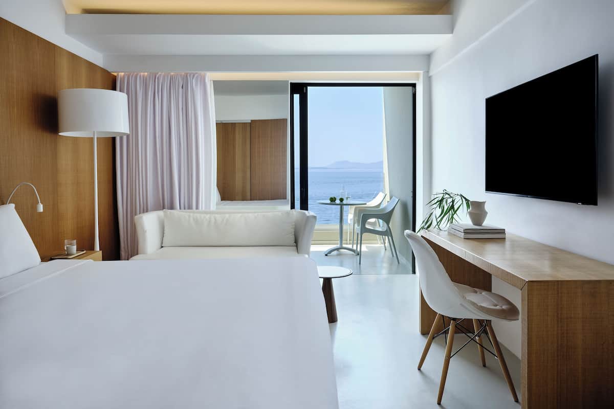 Une chambre d’hôtel moderne dotée d’un grand lit, d’un bureau, d’une télévision et d’un balcon offrant une vue sur la mer.