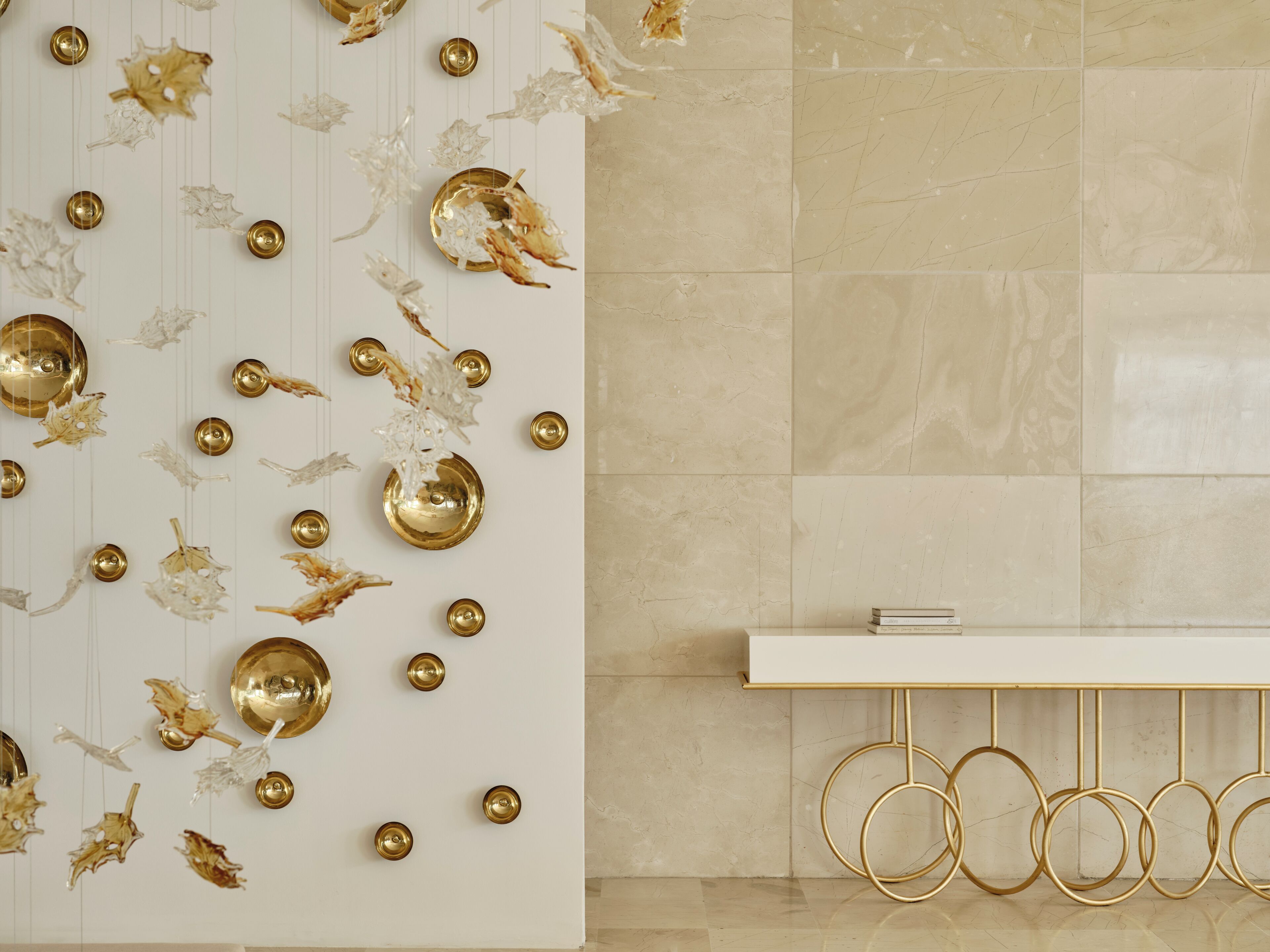 A modern interior with a white wall adorned with gold decorative elements and a white console table with gold rings.