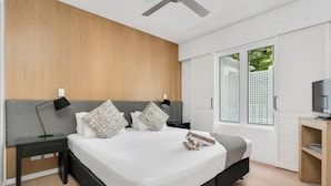 Un dormitorio moderno con una cama grande, dos mesitas de noche, un ventilador de techo y un televisor sobre un soporte de madera.
