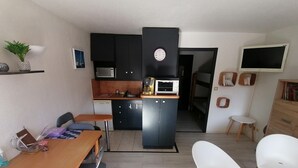 Een kleine keuken met een magnetron, broodrooster en spoelbak. Er is een eethoek met een tafel en stoelen. Een televisie is aan de muur bevestigd.