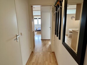Ein schmaler Flur mit Holzboden führt zu einem Schlafzimmer mit Bett und Fenster.