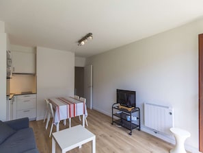 A compact living space with a kitchenette, a dining area with a striped tablecloth, a TV on a stand, and a radiator.