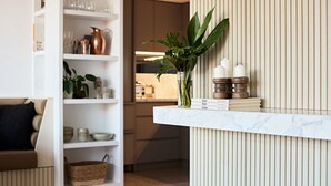 A kitchen with white cabinets, a marble countertop, and a shelf with books, candles, and a plant. - Fox on Macleay is a Two Bedroom Apartment (Elizabeth Bay)