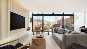 A modern living room with a large TV, comfortable seating, and a view of the cityscape. - Fox on Macleay is a Two Bedroom Apartment (Elizabeth Bay)