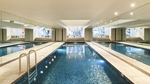 A large indoor swimming pool with clear water, surrounded by glass walls and a modern architectural design. - Fox on Macleay is a Two Bedroom Apartment (Elizabeth Bay)