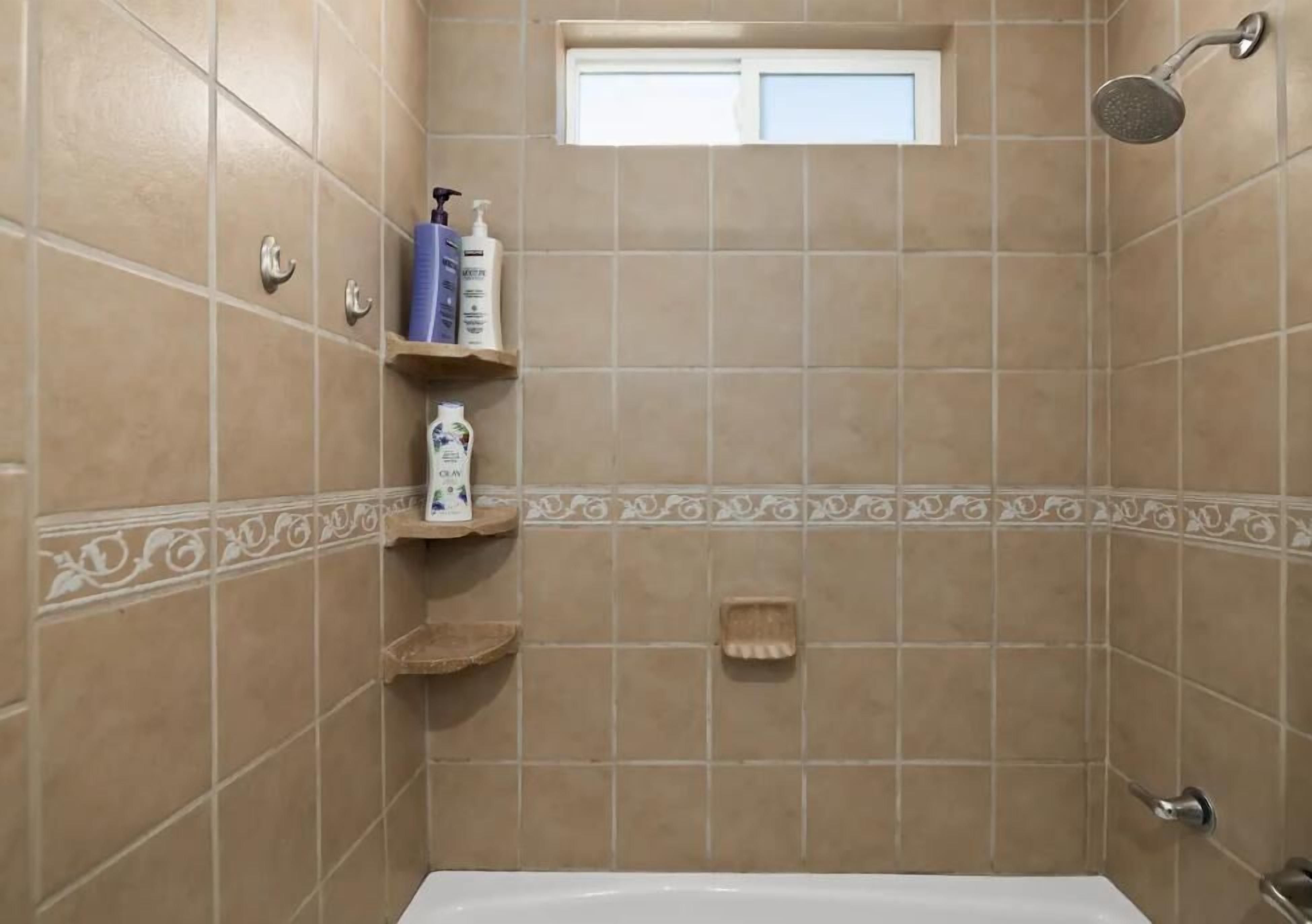 Ein Badezimmer mit beigen Fliesen, einer Dusche, einer Toilette und einem kleinen Fenster.