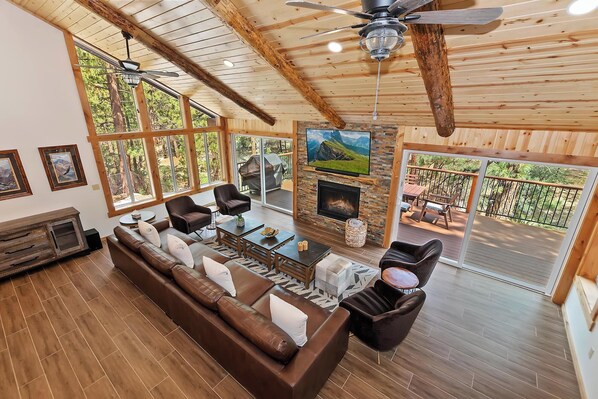 A spacious living room with a large sofa, a fireplace, and a television mounted on the wall.