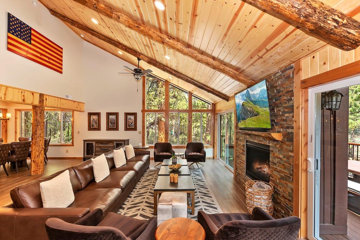 A spacious living area with a leather sofa, a fireplace, and a large window overlooking a forested area.