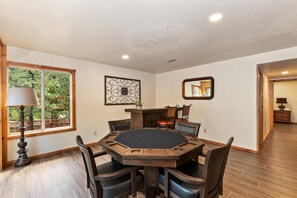 A round dining table with eight chairs, a window with a view of greenery, a decorative wall piece, and a mirror.
