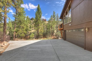 A residential property with a garage, a driveway, and a forested hillside. - Gold Rush Lodge: Exceptional Location in Big Bear's Eagle Mountain Estates! Luxury 5 En Suite Bedrooms! EV Charger! Pet Friendly! (Big Bear Lake)